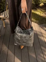 Cartera bandolera de gran tamaño en símil cuero color marrón con efecto desgastado. Cuenta con asa corta fija, correa larga regulable y placa metálica con logo en la parte frontal.