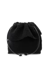 Bolso tipo saco (drawstring) de color negro, con cuerpo principal de material liso y solapa superior de textura borreguito o sherpa. Se cierra mediante un cordón de cuero sintético negro que también funciona como asa.