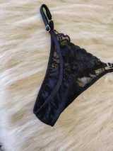 Conjunto de lencería compuesto por un bralette de encaje con breteles regulables y una tanga regulable con corte cola less. Ambas piezas presentan un diseño de encaje floral negro.