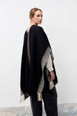 Ruana de tejido de punto en color negro, con diseño de guardas geométricas en tonos beige y blanco en los bordes y terminación con flecos.