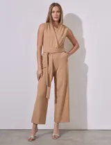 Mono color beige de crepe, marca Sharagano. Escote en V cruzado, sin mangas, con cintura elastizada y lazo de ajuste. Abertura central en espalda con cierre invisible y doble abotonadura. Bolsillos inclinados en delantera con aplique de botones.