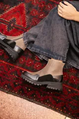 Bota corta de estilo urbano con diseño bicolor, combinando paneles de gamuza en color arena y cuero negro en la puntera y el talón. Cuenta con suela track de goma negra y cierre lateral.