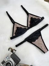 Conjunto de lencería compuesto por un corpiño triangular y una tanga, ambos confeccionados en lycra color beige con detalles de encaje negro y elásticos a tono.