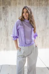 Blusa lila de cuello alto y manga 3/4 con elástico en el bajo. Presenta volados verticales en el frente.