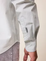 Camisa de manga larga en color blanco, confeccionada en algodón. Presenta cuello abotonado, cierre frontal con botones y un bolsillo en el pecho.