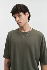 Remera oversize verde militar de manga corta y escote redondo, con estampado trasero de una cara sonriente amarilla con detalles en negro y texto "mistral 1976co".