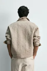Cazadora de corte regular confeccionada en tejido de algodón con textura jacquard floral. Presenta cuello solapa, manga larga, cierre frontal con botones y bolsillos laterales de vivo.