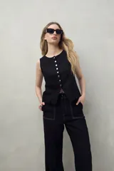 Pantalón negro de corte recto y tiro alto, confeccionado en denim con costuras a contratono en color blanco. Presenta bolsillos frontales tipo parche y cierre frontal con botón y cremallera.