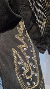 Campera de jean negra, corte a la cintura, con bordados decorativos, tachas plateadas y flecos de cadenas en la parte frontal y en las mangas.
