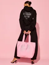 Bolso tote de canvas color rosado con diseño gráfico de alas adornado con pedrería, doble asa superior y cierre de botón a presión.