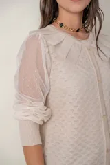 Cárdigan color beige con botones de strass, cuello de tul y mangas de plumeti.