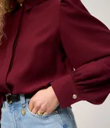 Camisa de crepé color blanco, con cuello inglés, manga larga abullonada con puños abotonados y cierre frontal oculto con botón diferenciado en el cuello.