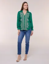 Camisa de estilo boho, color verde, con cuello camisero, escote en V y botonadura frontal con botones perlados. Cuenta con una pechera con bordados geométricos y florales a contraste, mangas largas abullonadas con puños abotonados y delicados bordados dispersos.