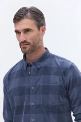 Camisa de manga larga confeccionada en viyela de algodón con diseño a cuadros en tonos verde oscuro. Presenta cuello clásico, cierre frontal con botones y bolsillo aplicado en el pecho.