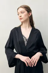 Bata de pijama negra de tejido satinado con leve elasticidad, silueta fluida y estilo envolvente. Presenta diseño cruzado con lazo regulable en la cintura y mangas amplias.