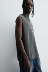 Sudadera sin mangas (tipo chaleco) de color gris oscuro con efecto lavado, corte relajado y cuello redondo. Presenta un estampado frontal en color rosa neón con texto y gráficos abstractos.