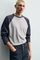 Camiseta de corte relajado con diseño color block, cuerpo en gris melange y mangas largas raglán en color azul marino. Presenta cuello redondo al tono de las mangas y bajo con acabado irregular.