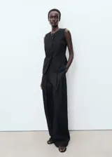 Chaleco sastrero negro sin mangas, con cuello redondo, tirantes anchos, diseño recto y cierre delantero con botones.