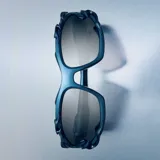 Lentes de sol con montura envolvente de color azul metalizado, con detalles decorativos de líneas orgánicas en los laterales. Cuentan con lentes de nylon en color gris y protección UV400.