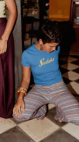 Remera tipo crop top de color azul con estampa frontal en color amarillo que dice 'Sudaka'. Presenta un ajuste entallado y cuello redondo.