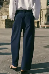 Pantalón barrel color azul marino, de tiro bajo, pernera holgada con diseño redondeado que se estrecha hacia el tobillo, con bolsillos delanteros y cierre frontal.