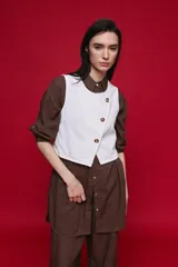 Chaleco blanco de denim con diseño cruzado asimétrico y cierre frontal con tres botones carey.