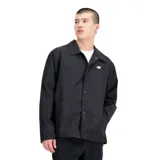 Campera negra tipo coach de New Balance, con cierre de botones a presión, corte relajado, mangas largas y logo blanco estampado en el pecho.