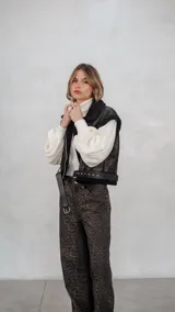 Chaleco de eco cuero negro con interior de corderito sintético, diseño oversize, cierre frontal y cinturón ajustable en el ruedo.