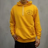 Canguro amarillo con capucha y cordones blancos, bolsillo tipo canguro y estampado frontal con texto y calavera.