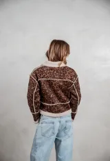 Campera de gamuza con estampado animal print de leopardo, forrada en corderito sintético color crema. Presenta cierre frontal con botones tipo toggle, cuello solapa y detalles de costuras visibles.