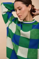 Buzo oversized de punto texturizado, con diseño a cuadros en tonos de verde, azul y blanco. Tiene cuello redondo y puños acanalados.