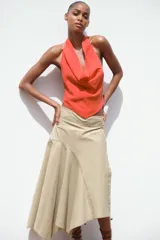 Top de color naranja vibrante con cuello halter que se anuda en la espalda, creando un escote drapeado o fluido en el frente. El bajo del top tiene un corte en pico con tiras finas colgantes.