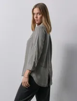 Camisa gris de tencel con cuello con solapa, escote en V y abertura central con botones. Largo de manga regulable con presilla y botón. Ruedo en espalda con tajo.