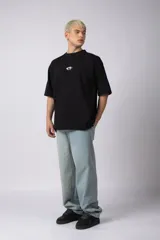 Remera de corte oversize confeccionada en algodón pesado, color negro. Presenta un bordado minimalista en el centro del pecho con forma de ojo y un parche estampado en la espalda que ilustra una mano abriendo una persiana.
