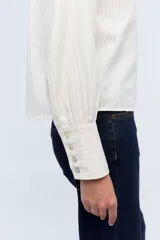 Camisa color crema a rayas verticales finas, con cuello mao con lazos para atar, escote en V y mangas largas con puños abotonados.