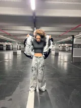 Conjunto de saco y pantalón plateado con estampado de flores negras. El saco es de corte deportivo con cierre y volados en el cuello y mangas. El pantalón es de corte ancho.