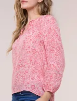 Blusa holgada de gasa liviana con estampado floral en tonos rosados y blancos. Presenta escote en V con muesca central y mangas largas abullonadas con inserción de puntilla y puños elastizados.