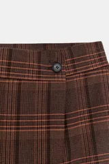 Bermuda de tiro medio con diseño cruzado frontal y cierre de botón. Presenta un estampado de cuadros en tonos marrones y rojizos, con bolsillos delanteros y falso bolsillo trasero.