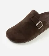 Ojota mule de cuero con acabado de gamuza color marrón, diseño cerrado en la parte delantera con hebilla metálica lateral ajustable y suela dentada de goma.
