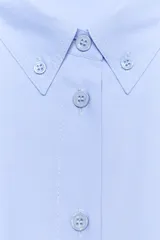 Camisa de manga larga color celeste claro, confeccionada en popelín de algodón. Presenta cuello solapa con botones y un bolsillo de parche en el pecho izquierdo.