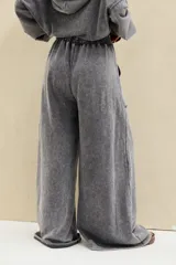 Pantalón gris con efecto acid wash, tiro alto con cintura elástica fruncida, corte amplio tipo palazzo y grandes bolsillos frontales aplicados.