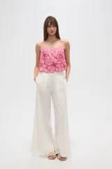 Top lencero de algodón color rosa claro, con tirantes finos y escote profundo. Presenta bordados florales grandes en color fucsia con detalles de mostacillas en el centro de las flores. El calce es holgado.