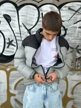 Campera puffer gris con sección superior negra y cierre frontal.