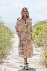 Túnica camisera de corte recto y largo midi, con cuello solapa y cierre frontal de botones. Presenta un estampado integral de guepardos y flores sobre fondo rosado.