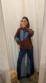 Campera tejida de hilo color marrón chocolate con cierre frontal y diseño de gran corazón azul en el centro. Cuenta con detalles bordados en los costados del pecho.