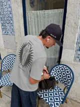 Remera gris de manga corta con corte regular, de la marca Kaboa Industries, con estampa en la espalda que presenta un esqueleto dentro de un ataúd rodeado por alas oscuras y las leyendas WAKE UP y Kaboa Industries.