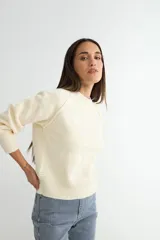 Buzo tejido de punto color crema, con cuello redondo, mangas largas con costuras raglán y puños y ruedo acanalados.