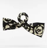 Pashmina de textura suave con diseño estampado de camelias en contraste blanco y negro. Presenta bordes con flecos cortos.