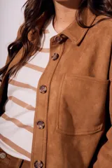 Sobrecamisa negra de estilo shacket, confeccionada en tejido de gamuza sintética. Presenta cuello camisero, cierre frontal de botones y dos bolsillos de parche con solapa en el pecho. El calce es oversize y las mangas son largas.