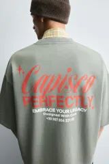 Sudadera de corte boxy fit, color verde oliva con efecto lavado. Presenta cuello redondo, manga corta terminada en rib y textos estampados a contraste en color rojo en el pecho.